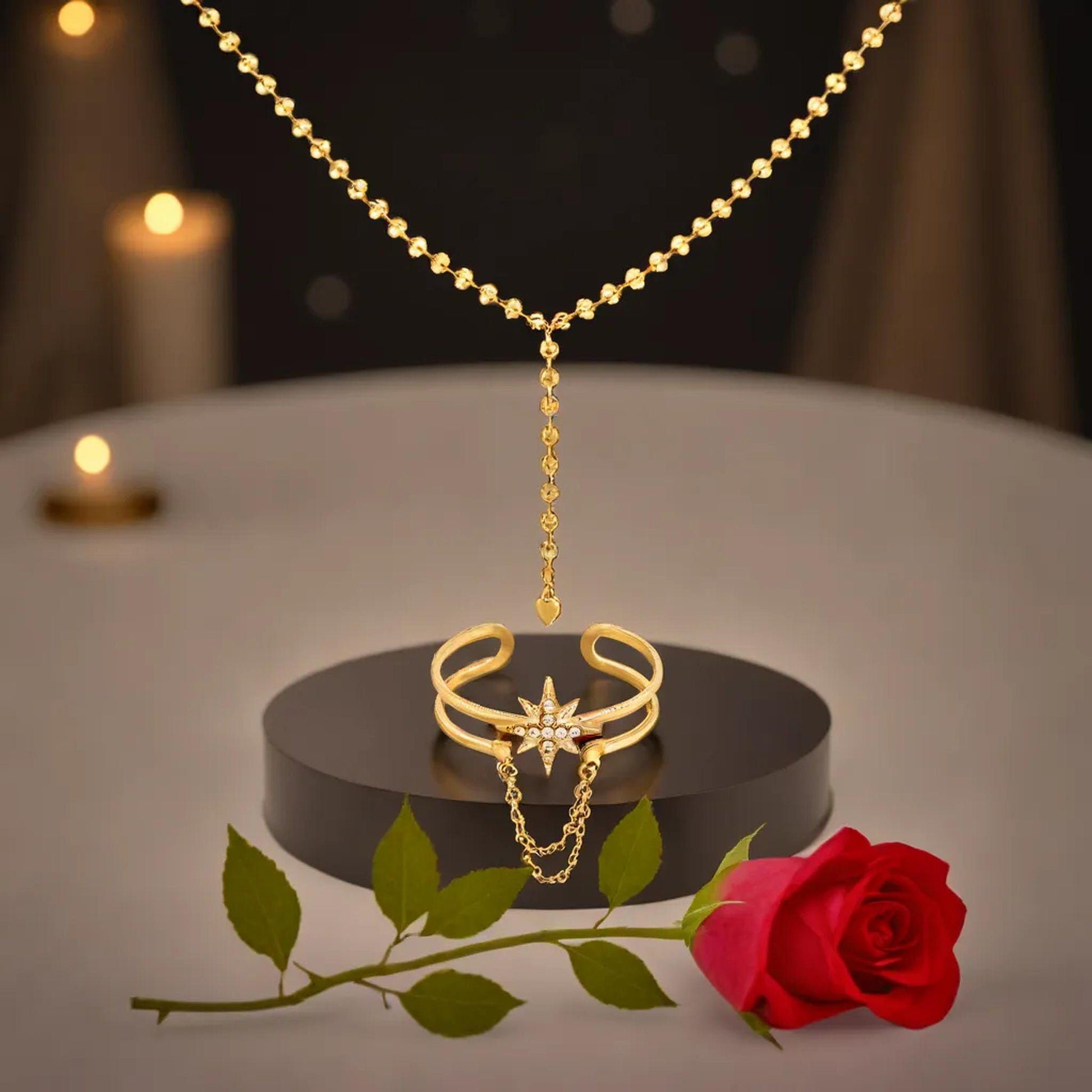 Goldener Sternring und Halskette als Set, präsentiert auf schwarzem Sockel, umgeben von Rosen und sanft leuchtenden Kerzen.