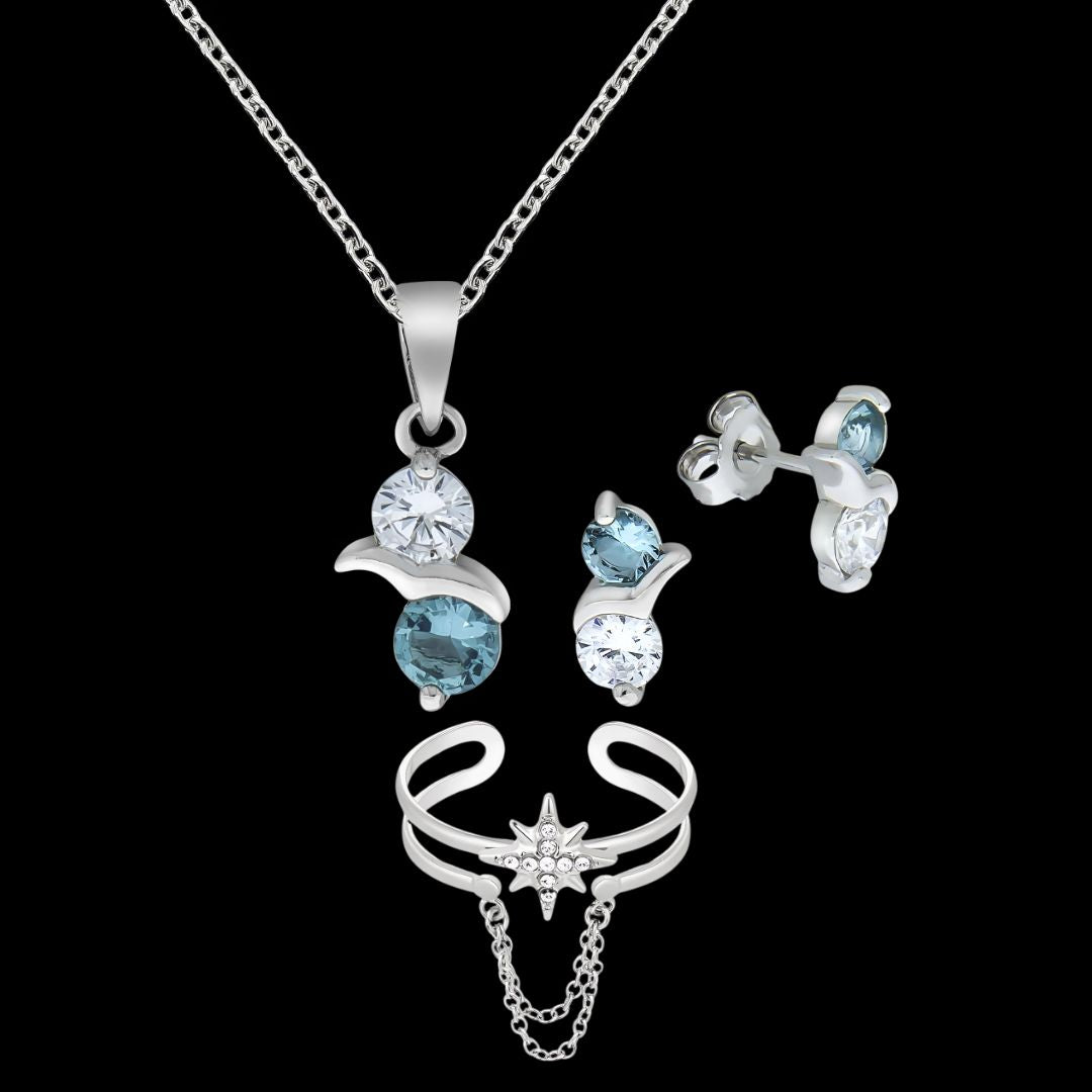 Vor schwarzem Hintergrund ist ein Schmuckset abgebildet. Oben hängt eine silberne Halskette mit einem runden, klaren und einem blauen Stein, darunter ein Paar passende silberne Ohrstecker mit denselben Steinen. Unter dem Set ist ein silbener, offener Fingerring mit Sternmotiv und feinen, hängenden Kettchen zu sehen.